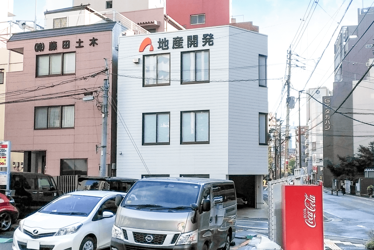 建物の前に駐車された車と「地産開発」と書かれた建物が写っている街の風景。